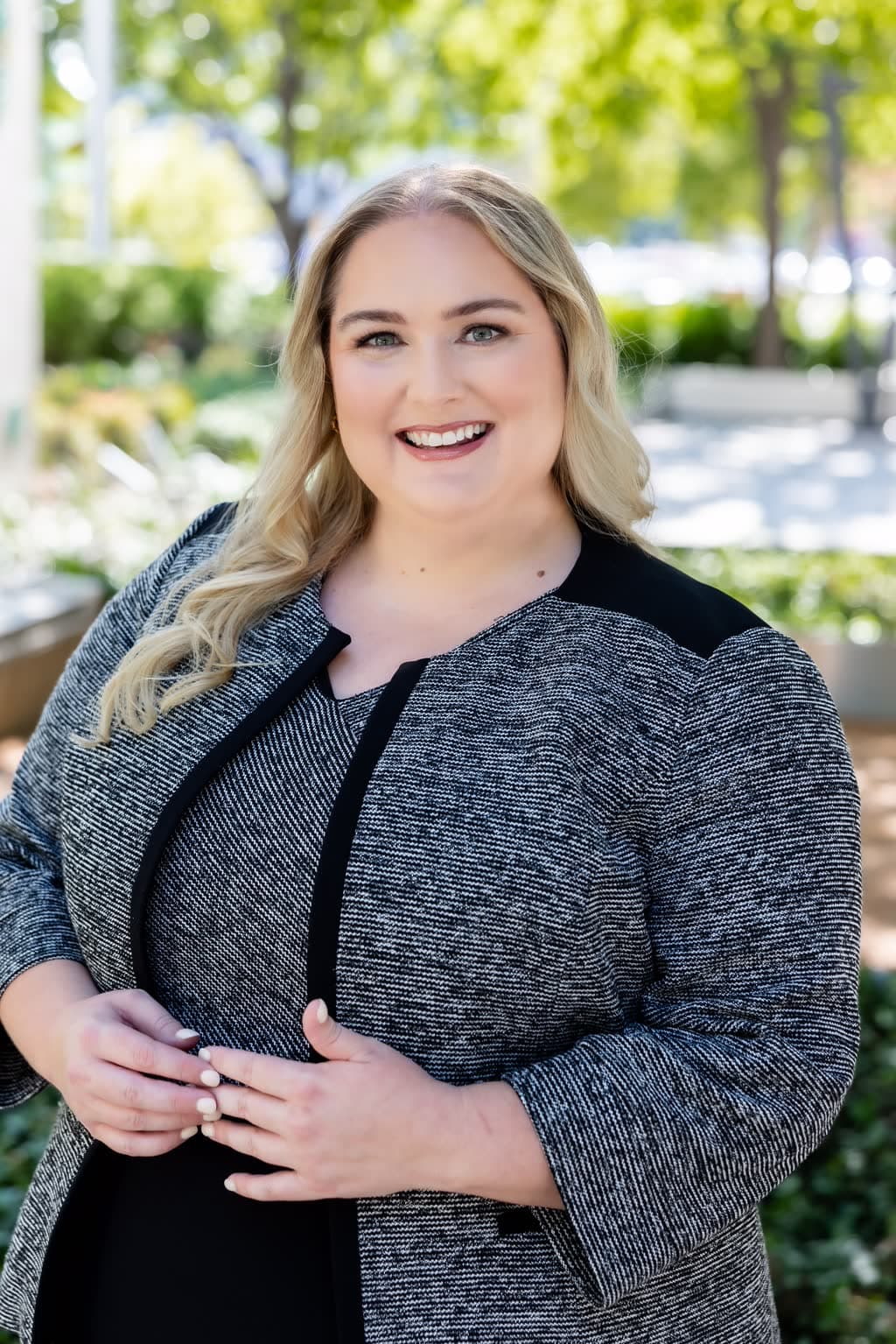 Caila M. Cleary smiling outdoors in a black and white tweed jacket