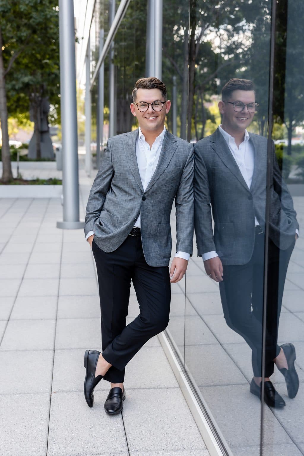 Joe Otanez in a gray jacket, leaning against a glass building that reflects his image