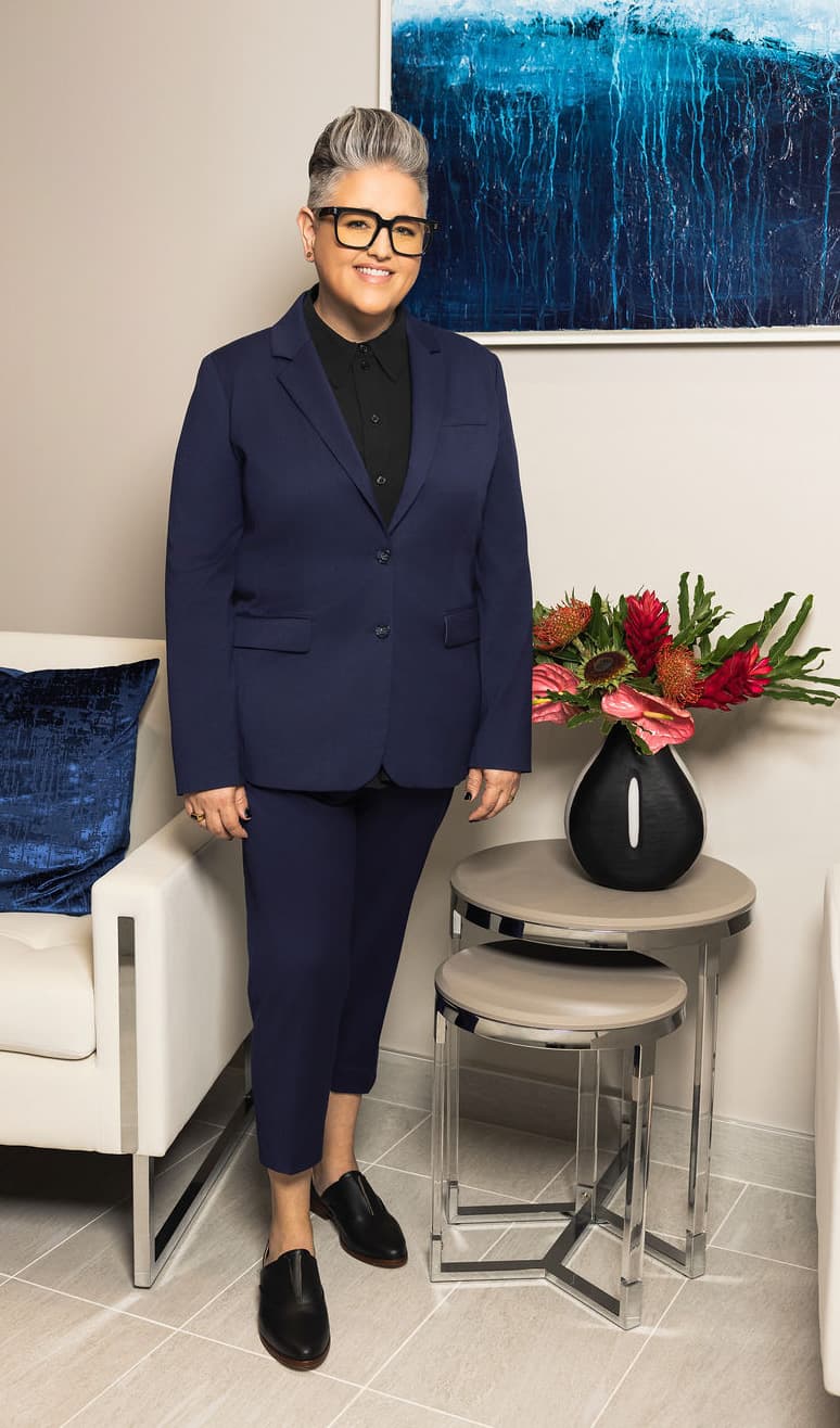 M.K. Kassie Hines standing in a modern office, professionally dressed in a navy suit